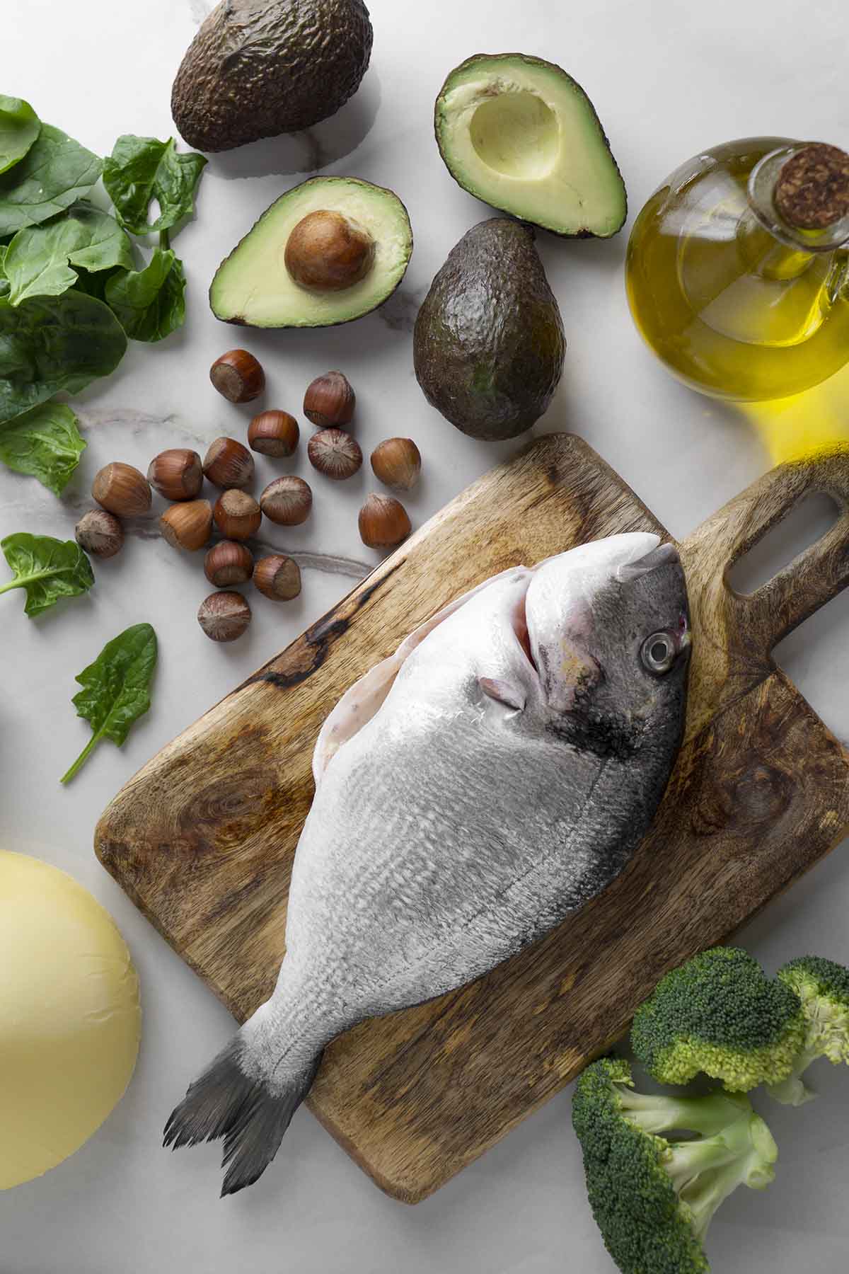 Натюрморт: свежая рыба дорадо с авокадо и брокколи на столе, готовая к приготволению. Вид сверху